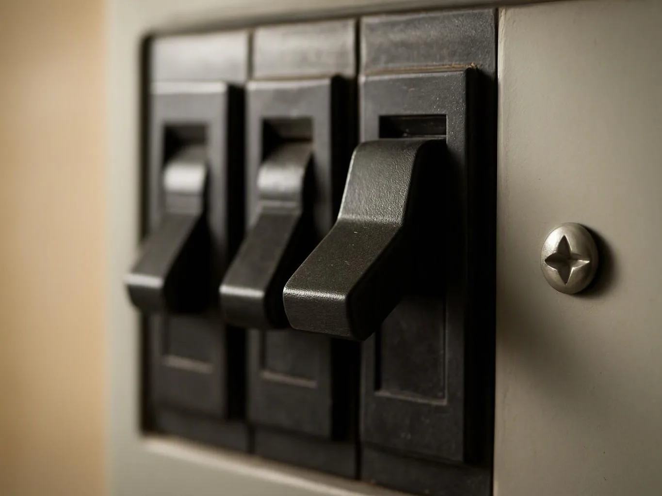 A close-up shows three black toggle switches on a wall plate beside a silver screw