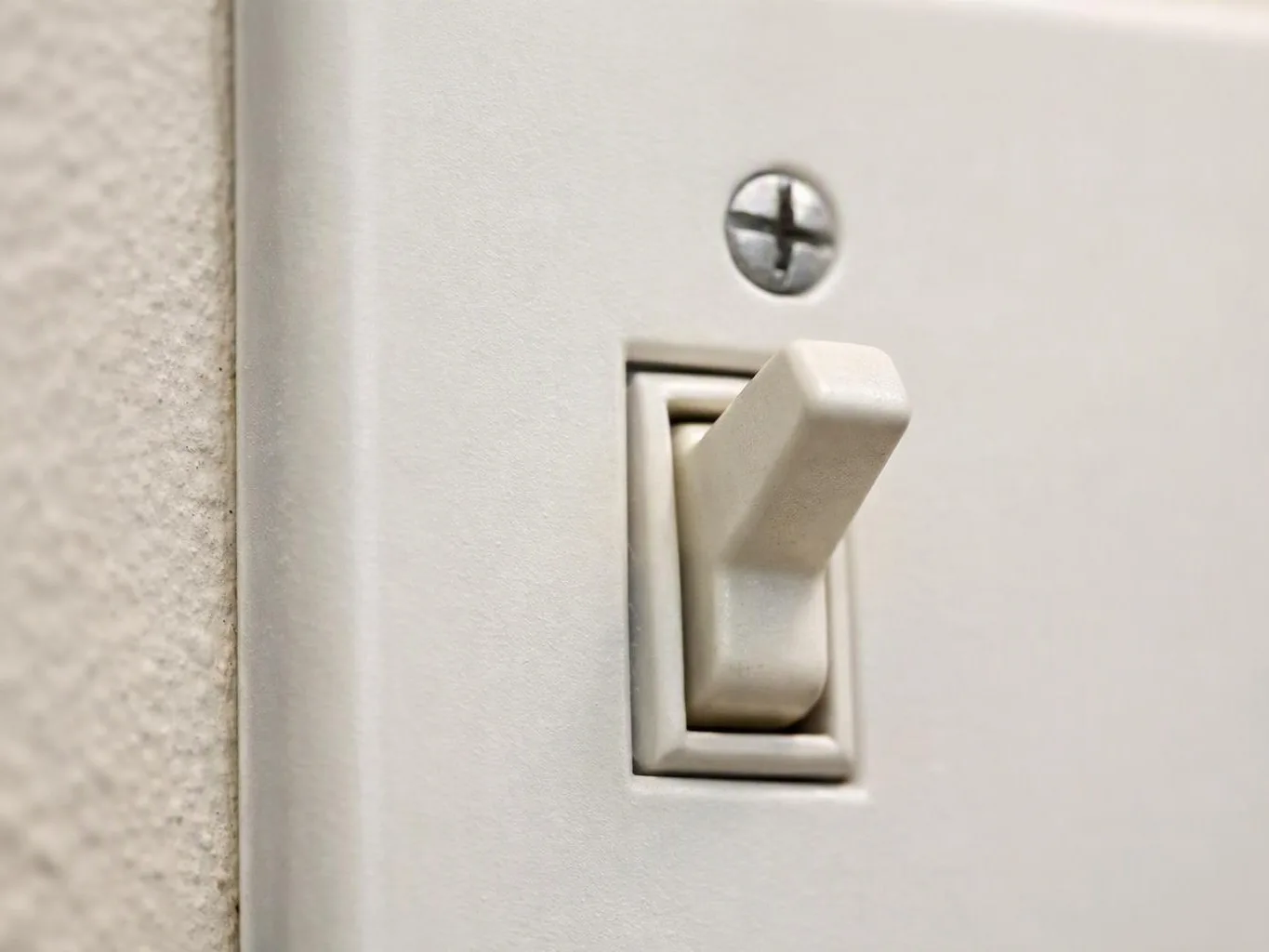 A close-up shows a white plastic light switch on a wall plate beside textured wall paint