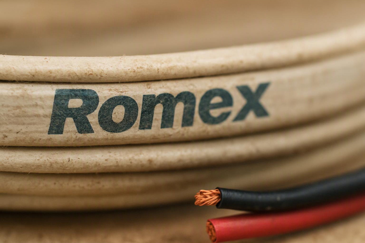 A coiled beige cable labeled Romex sits beside cut black and red wires on a work surface