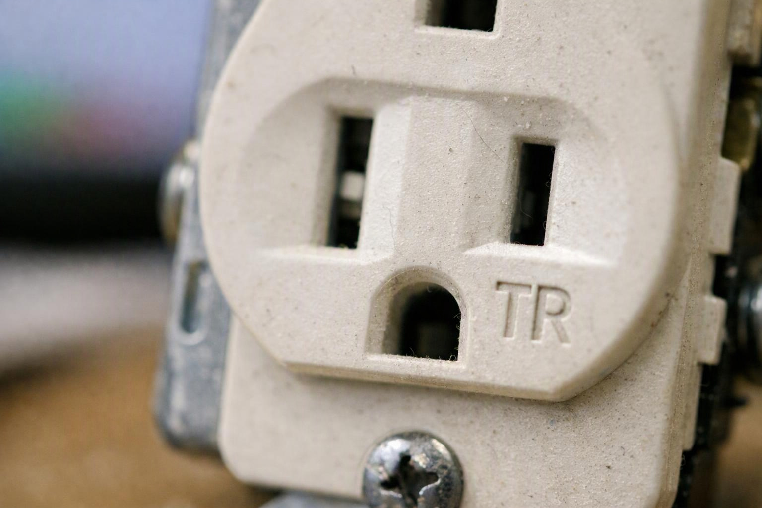 Close-up of a beige electrical wall outlet with two slots, a ground opening, and a visible screw